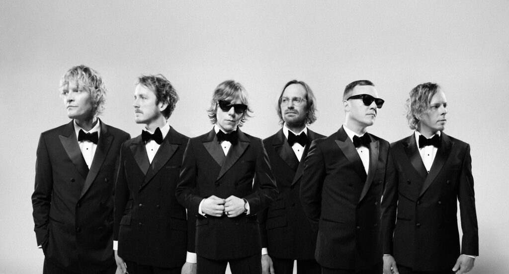 Black and white photo of the band with all its members wearing tuxedos.