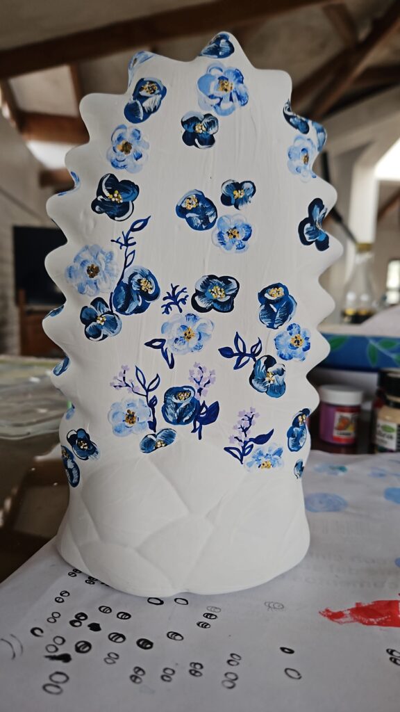 Fotografía de una figura de cerámica pintada con una base blanca, con flores de colores azules en diferentes tonalidades. 