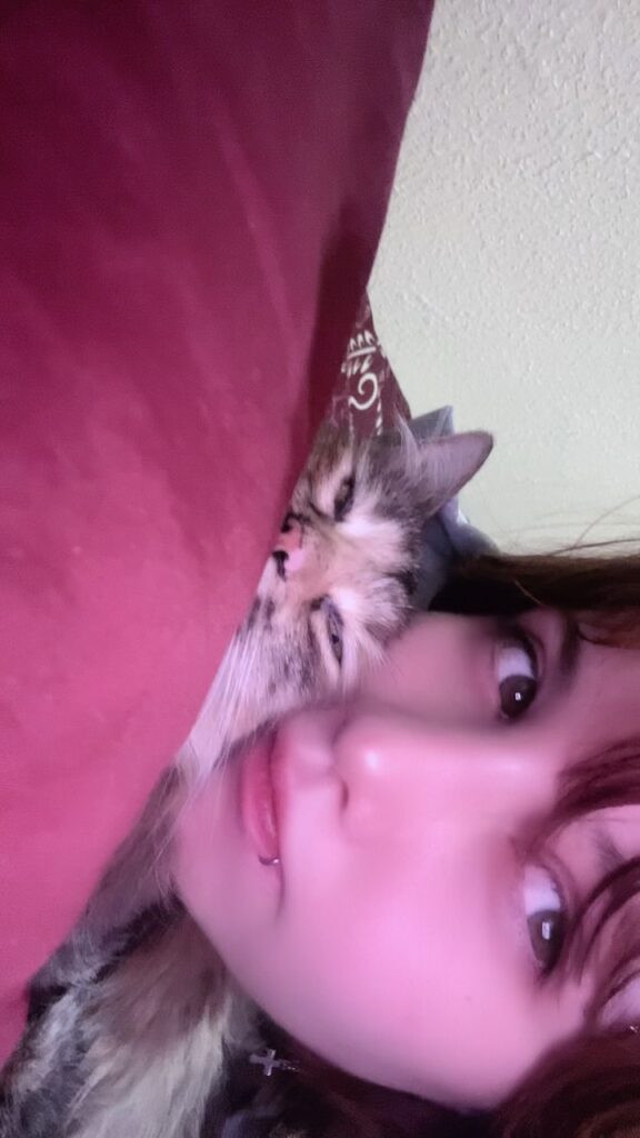 Una chica abrazando levemente a su gata viendo casi a la cámara 