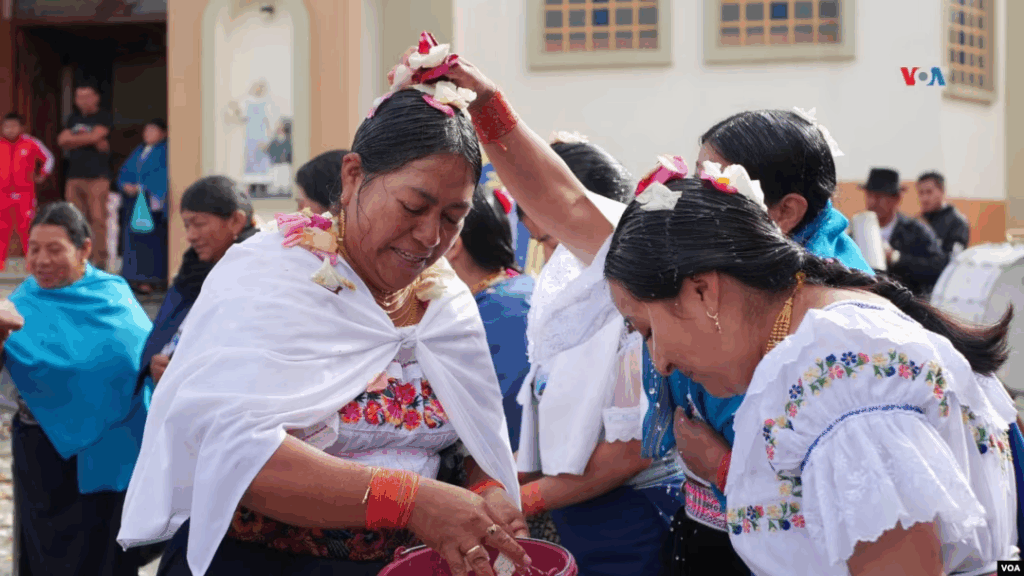 Two Indigenous women from Ecuador holding rose petals in their hands.