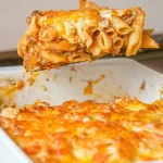 Bandeja blanca de macarrones reci&eacute;n hechos con una porci&oacute;n levantada con un cuchar&oacute;n.