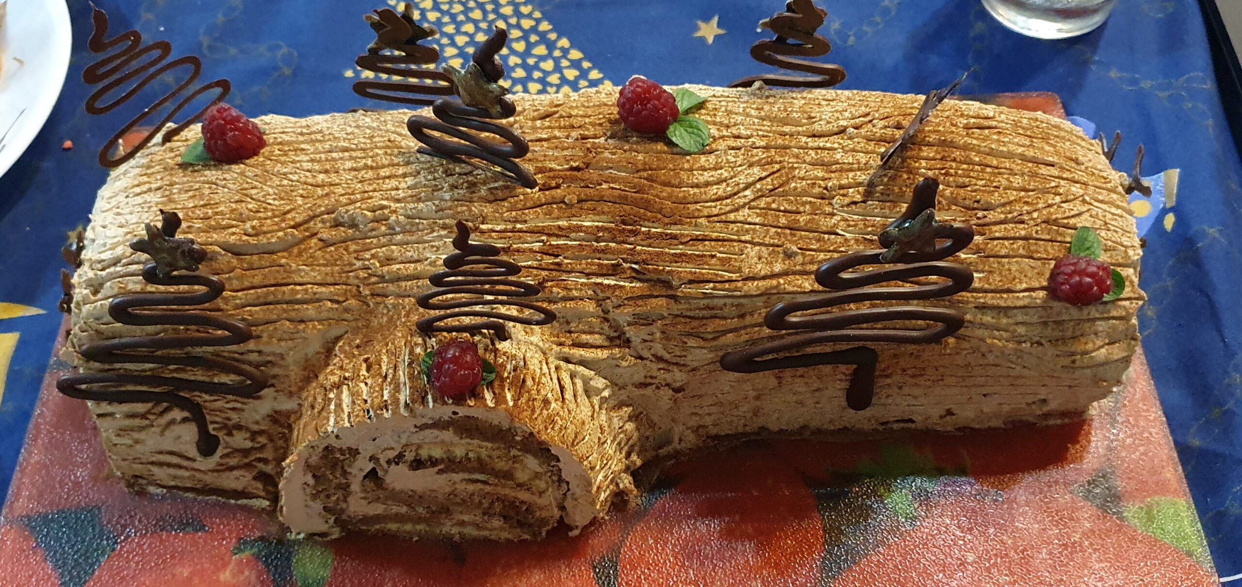 Fotografía de un tronco navideño  de café decorado con árboles de chocolate, frambuesas y hojas de menta.