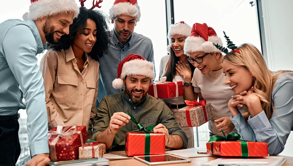 Group of friends gathered, watching as one of them opens their gift.
