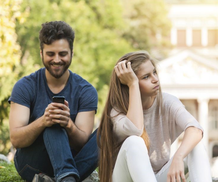 hay una pareja, un hombre y una mujer, los dos estan sentados, pero el hombre esta mirando su celular con una sonrisa y la mujer está viendo a lado contrariado con las mejillas como resoplando, su actitud parece estar cansada de la situación