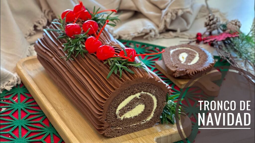 Fotografía de un tronco navideño de chocolate, decorado con cerezas marrasquino y ramas de romero.